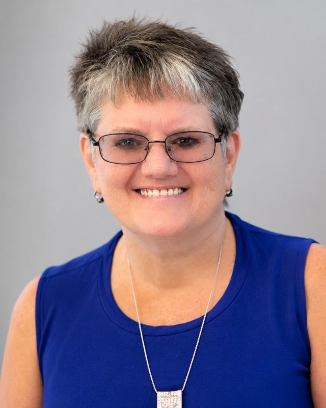 Debbie Thompson, 2026 Anthony Wayne Hall of Fame inductee, smiling in a royal blue sleeveless top against a light gray background.