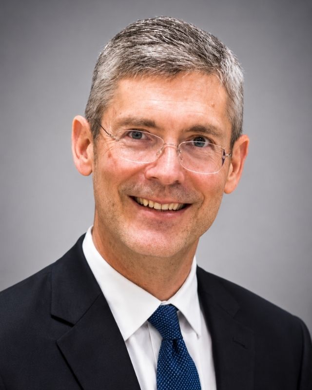 Kevin Click, 2026 Anthony Wayne Hall of Fame inductee, smiling in a dark suit and blue tie against a gray background.